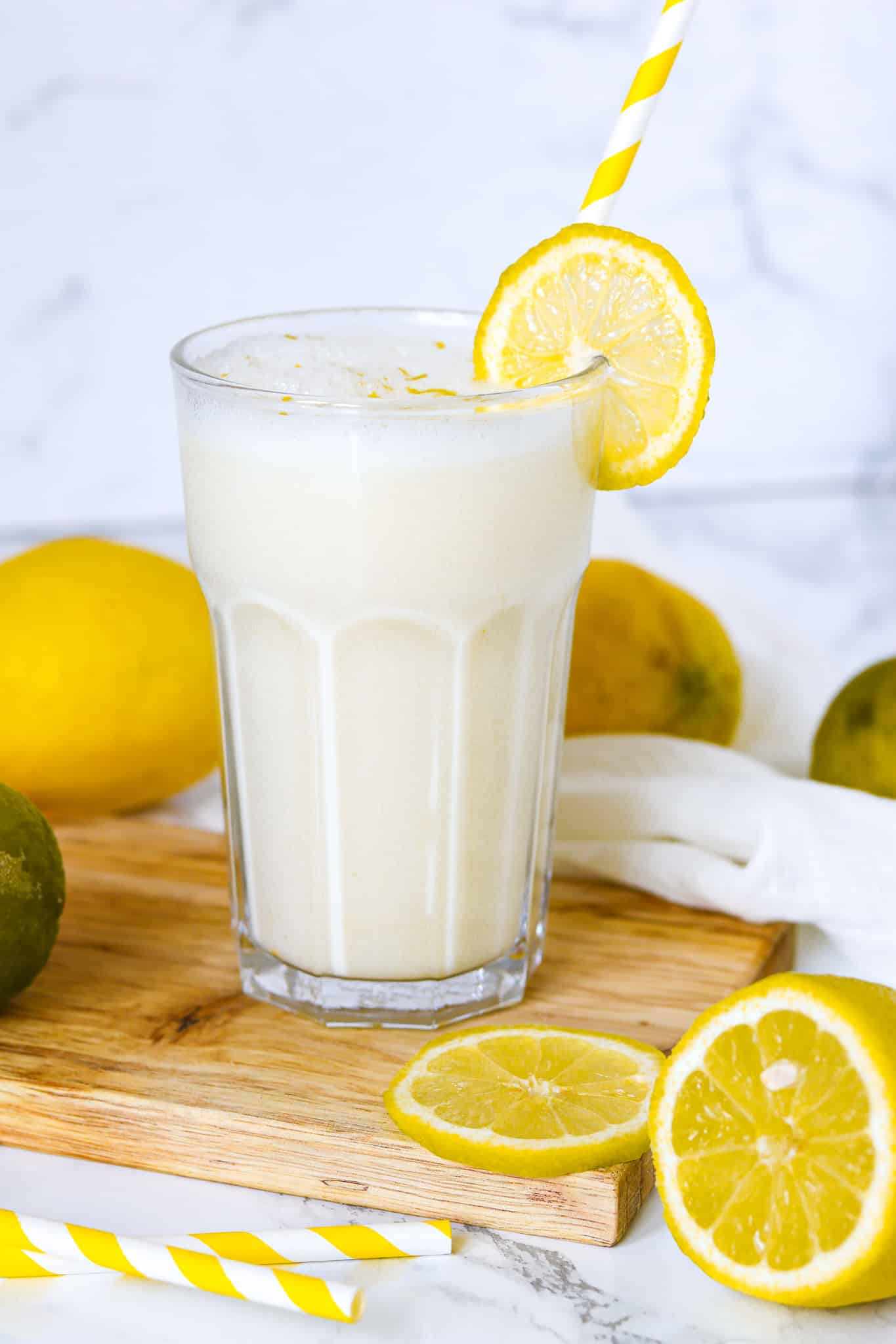 erfrischende Zitronenbuttermilch im Glas mit gelbem Strohhalm und Zitronen