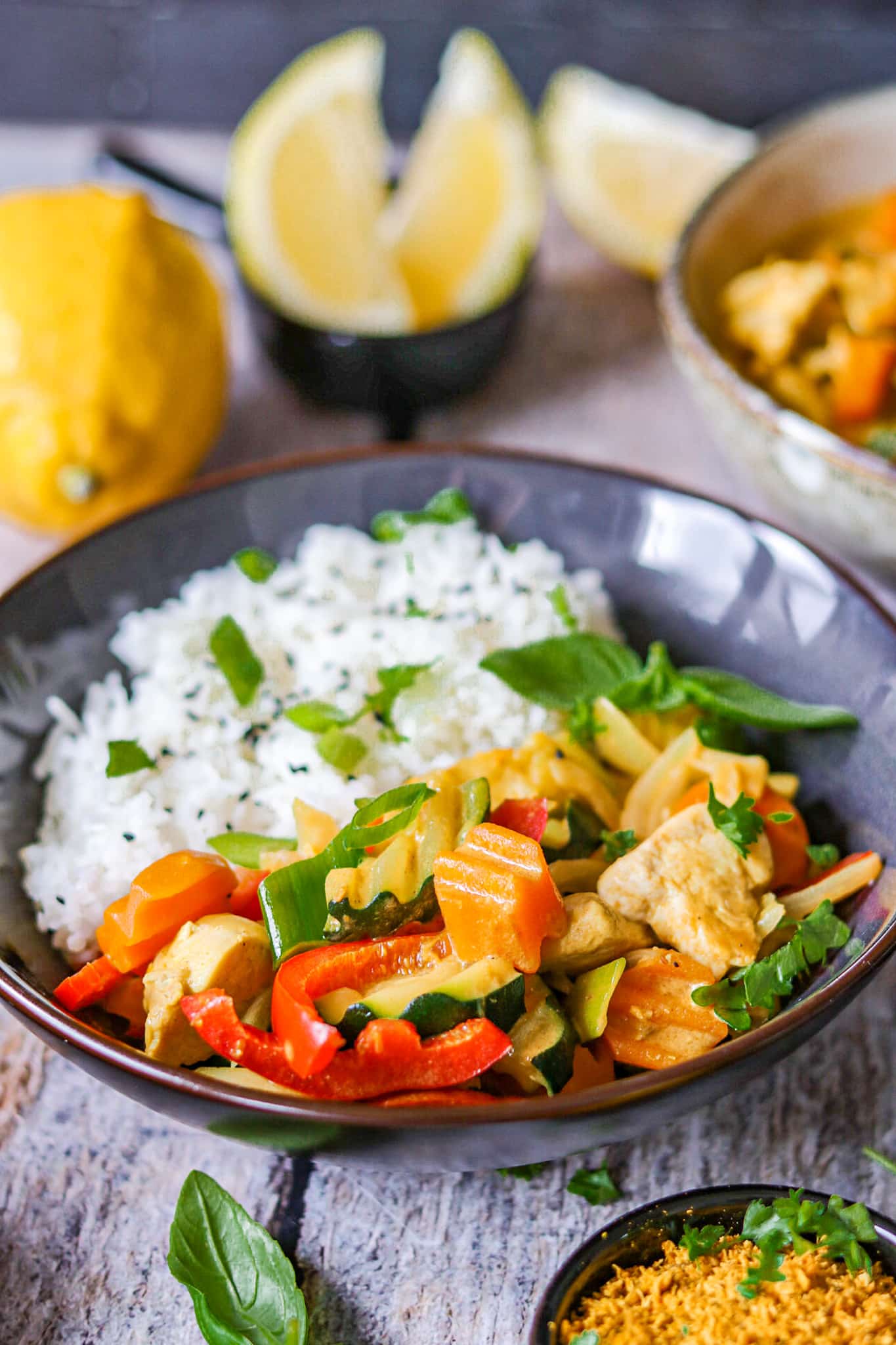 Hähnchen Curry mit Reis auf einem dunklen Teller mit Gewürzen und frischen Kräutern