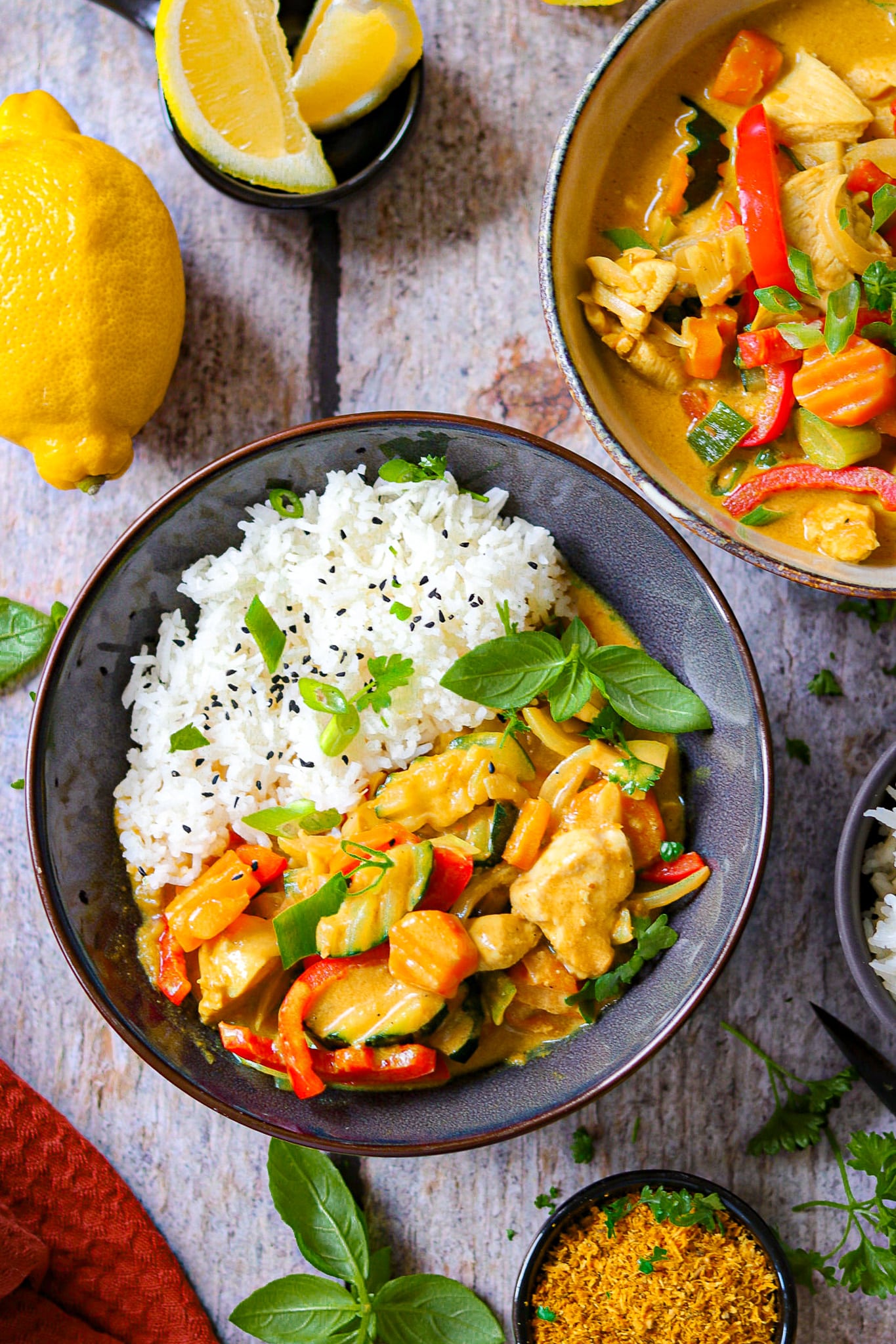 Hähnchen Curry mit Reis auf einem dunklen Teller mit Gewürzen und frischen Kräutern