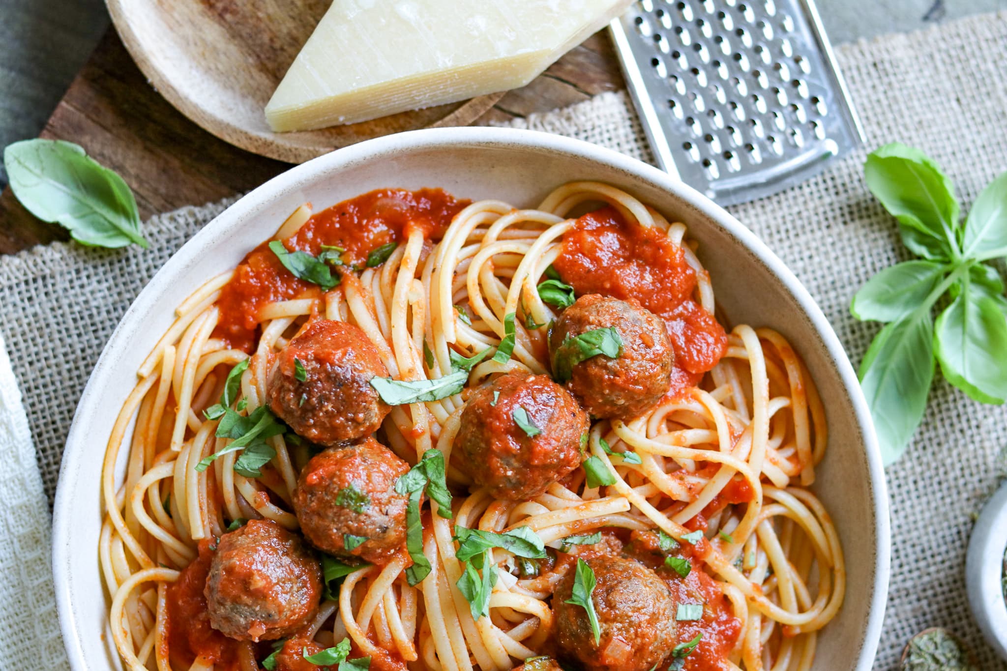 Spaghetti mit Fleischbällchen, mit frischem Basilikum auf einem hellen Teller mit Parmesan und Reibe