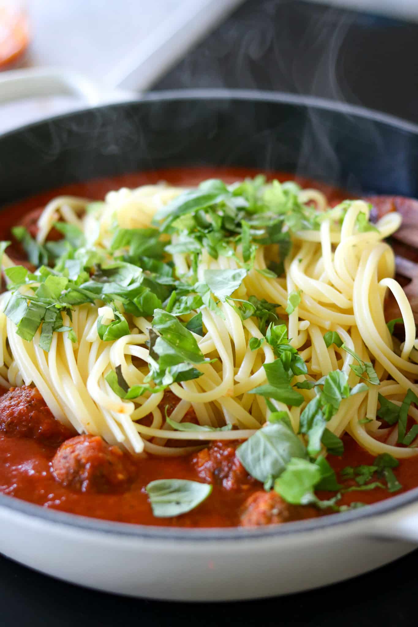 Spaghetti mit Fleischbällchen, Frische Tomatensoße mit der gekochten Pasta und Kräutern in einer Pfanne, noch nicht vermengt
