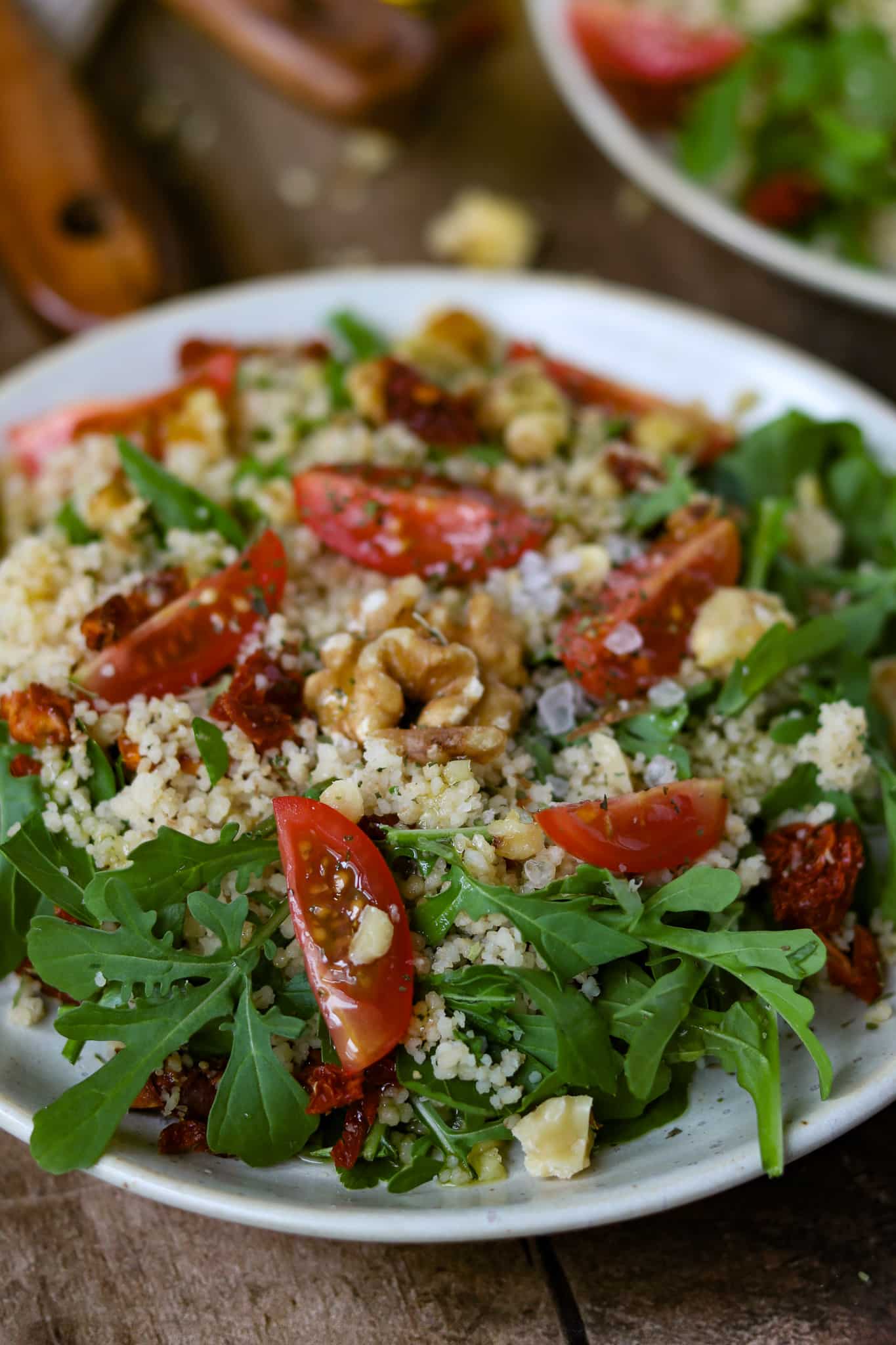 Couscous Salat Rezept, präsentiert auf einem hellen Teller auf einem rustikalen Holzbrett , man Erkennt den Couscous und einzelnen Tomatenstücken und ganzen Walnüssen