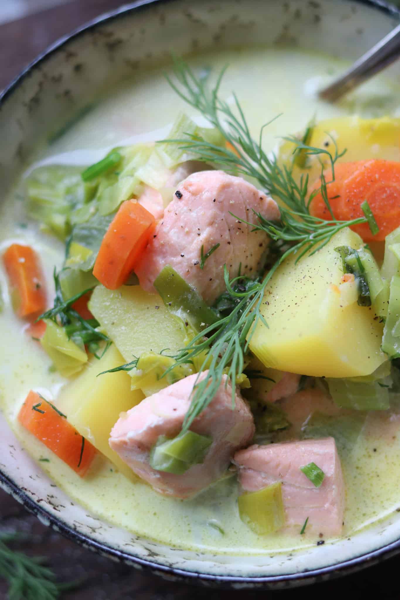 Fischsuppe mit Lachs, serviert in einen grau grünen Schüssel auf einem rustikalen Brett. Mit frischem Dill und Gemüse