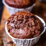Double Chocolate Muffins mit Papier und Schokoladenstückchen auf einem rustikalen Brett und dunklem Untergrund