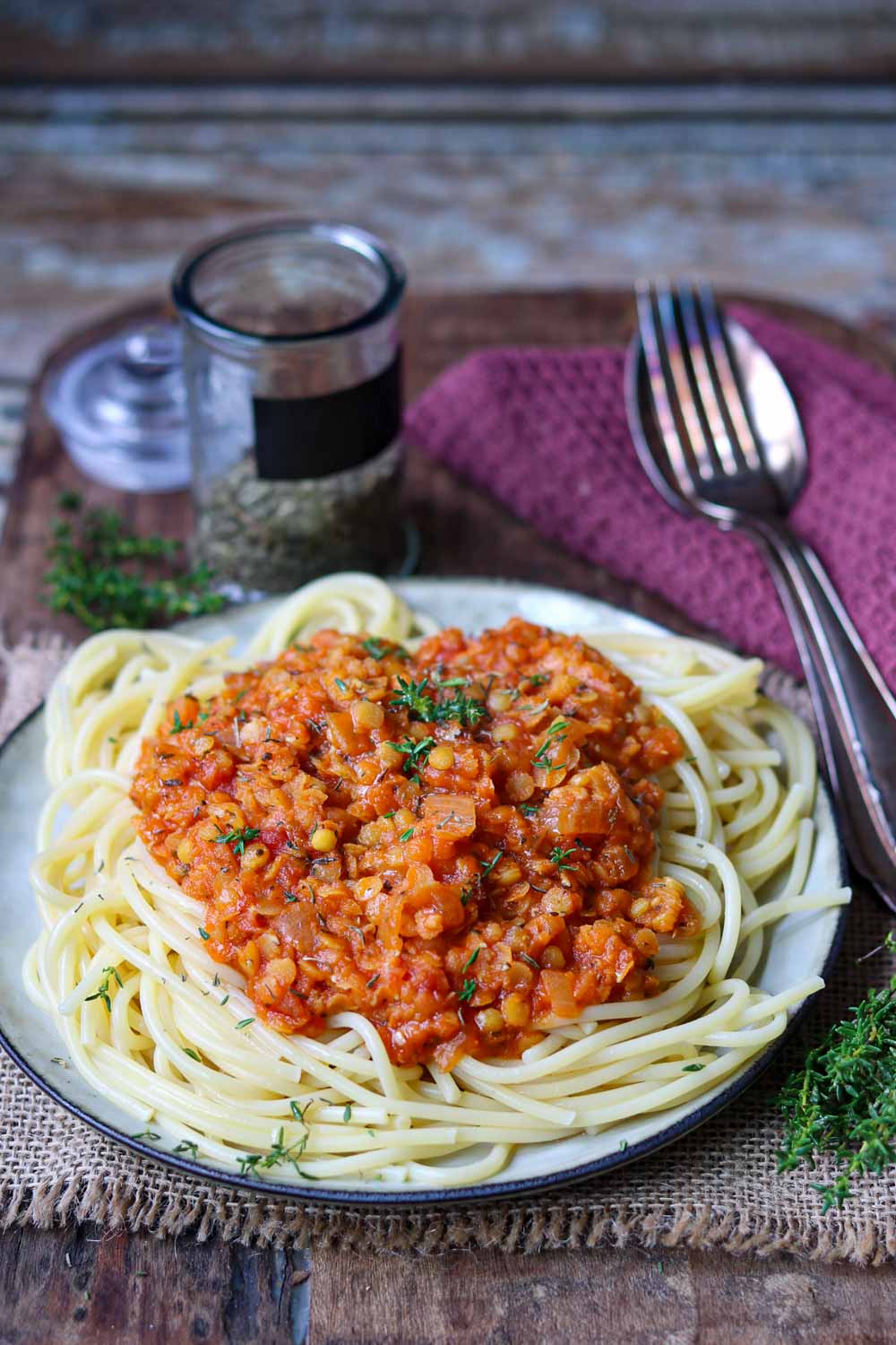 Spaghetti mit roter Linsenbolognese serviert auf einem Holzbrett mit thymian 