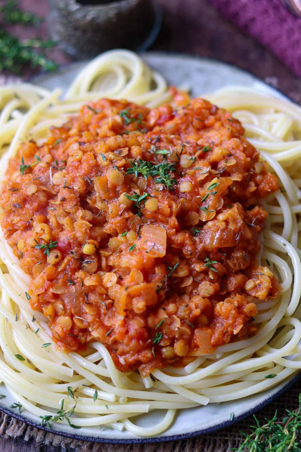 Spaghetti mit Linsenbolognese serviert auf einem Holzbrett, aus roten linsen mit frischen kräutern