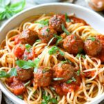 Spaghetti mit Fleischbällchen in Tomatensoße serviert auf einem hellen Teller mit frischen Kräuternt