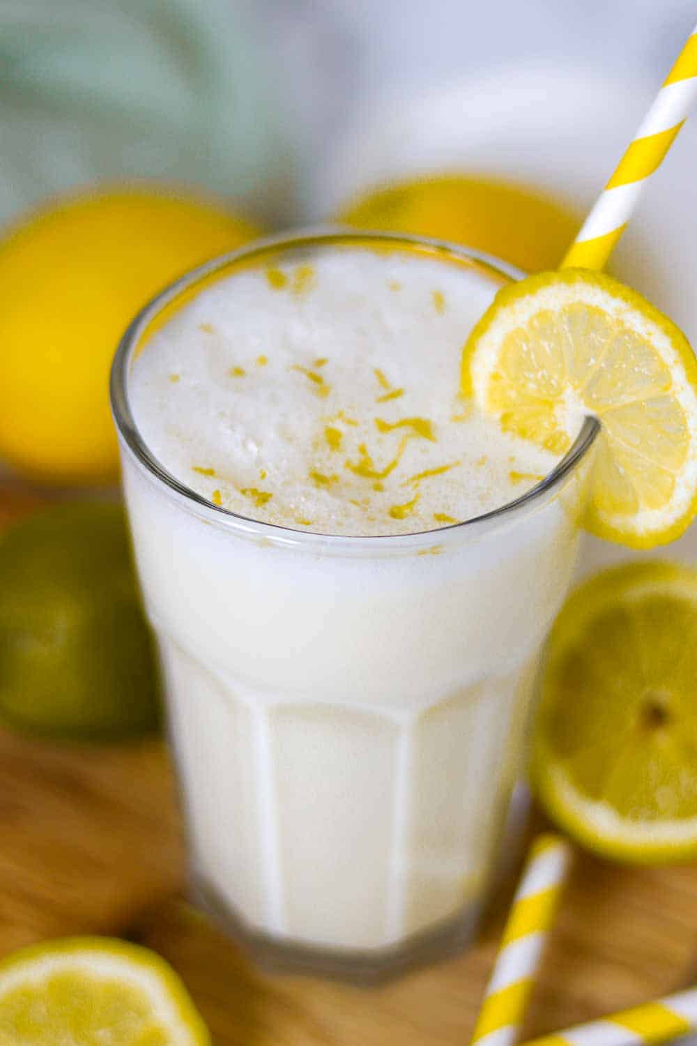 erfrischende Zitronenbuttermilch im Glas mit gelbem Strohhalm und Zitronen