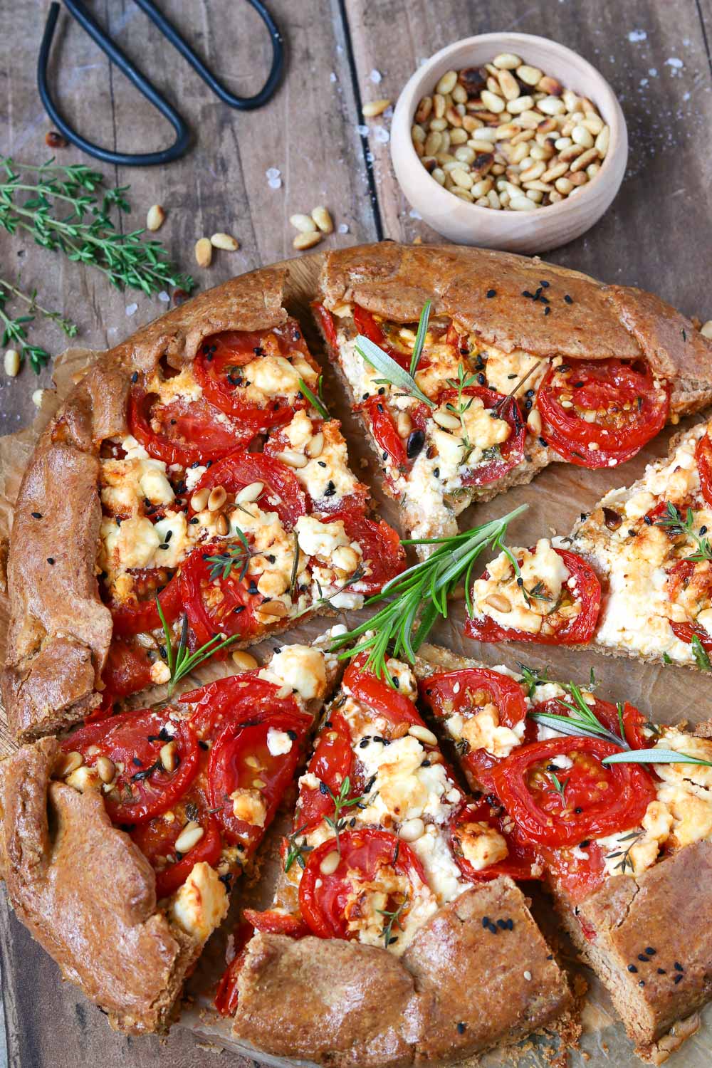 Tomatentarte – das einfache Sommerrezept, Tarte ist aufgeschnitten, Kräuter sind im Hintergrund