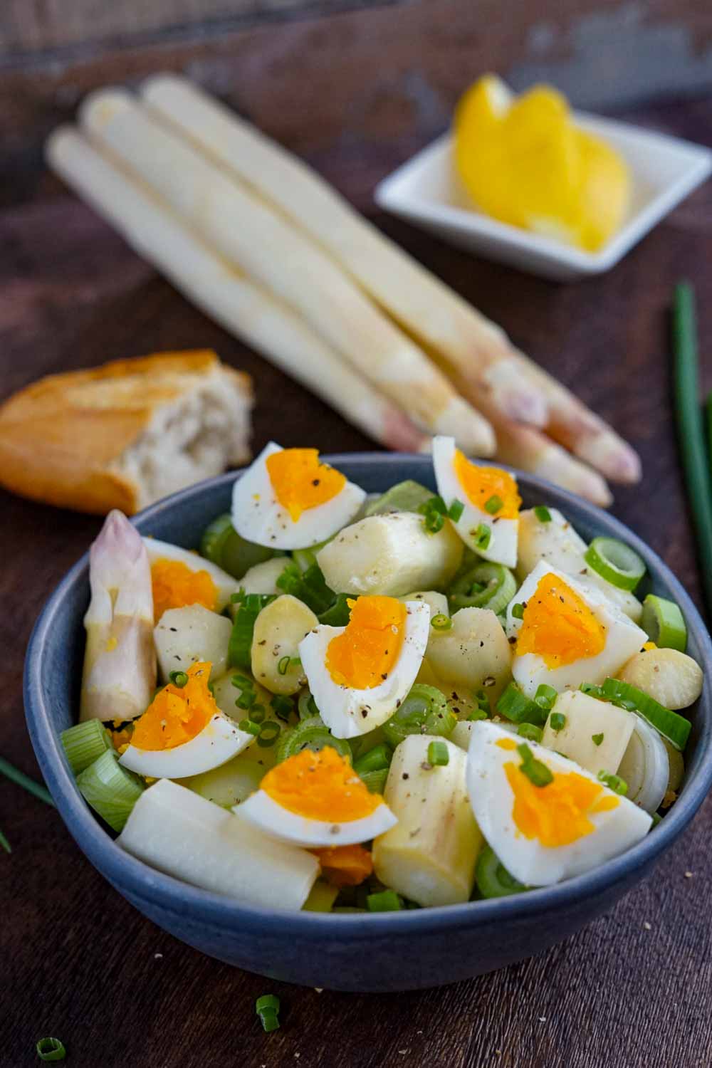 Spargelsalat mit Ei und Senf-Dressing serviert mit Frühligszwiebeln und Baguette