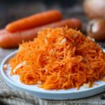 Karottensalat nach Omas Rezept serviert auf einem Teller und auf einem holzbrett