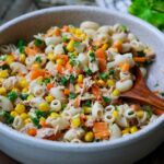 Nudelsalat mit Thunfisch mit Mais thunfisch und Käutern in einer hellen Schüssel mit Holzlöffel