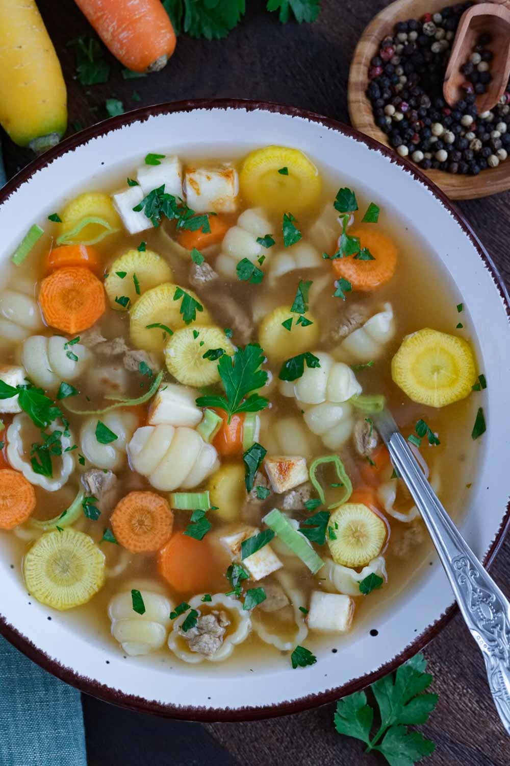 rindfleischsuppe mit gemüse serviert in einer hellen schlale und kräutern